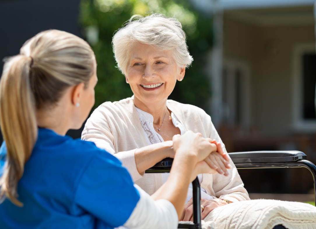 Uśmiechnięta seniorka na wózku rozmawia z opiekunką na świeżym powietrzu